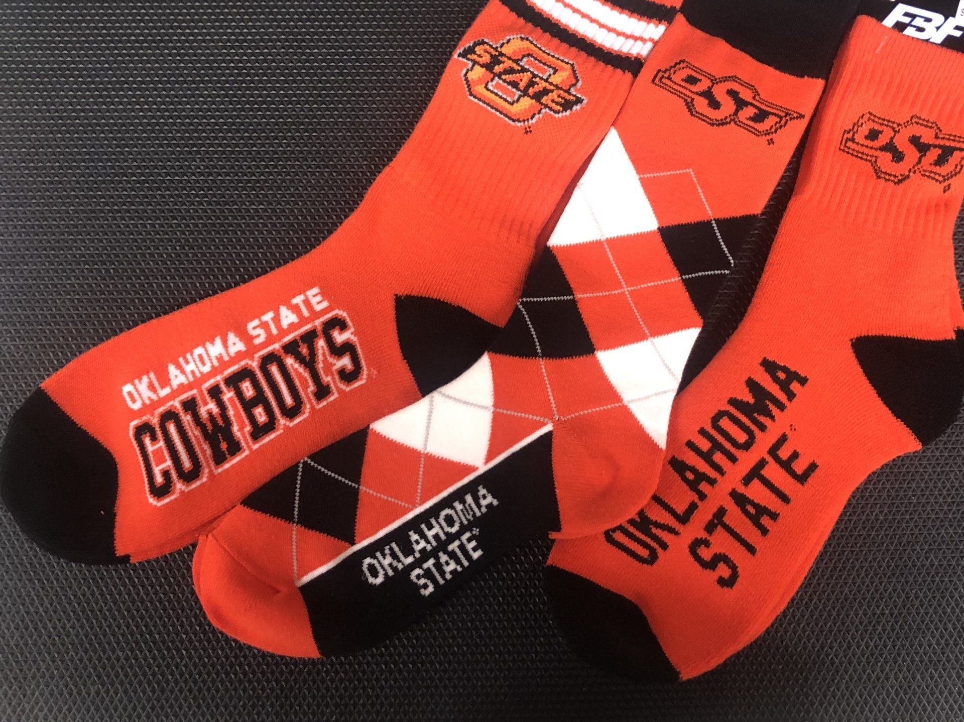 Three pairs of orange, black, and white Oklahoma State University socks displayed on a dark textured surface.