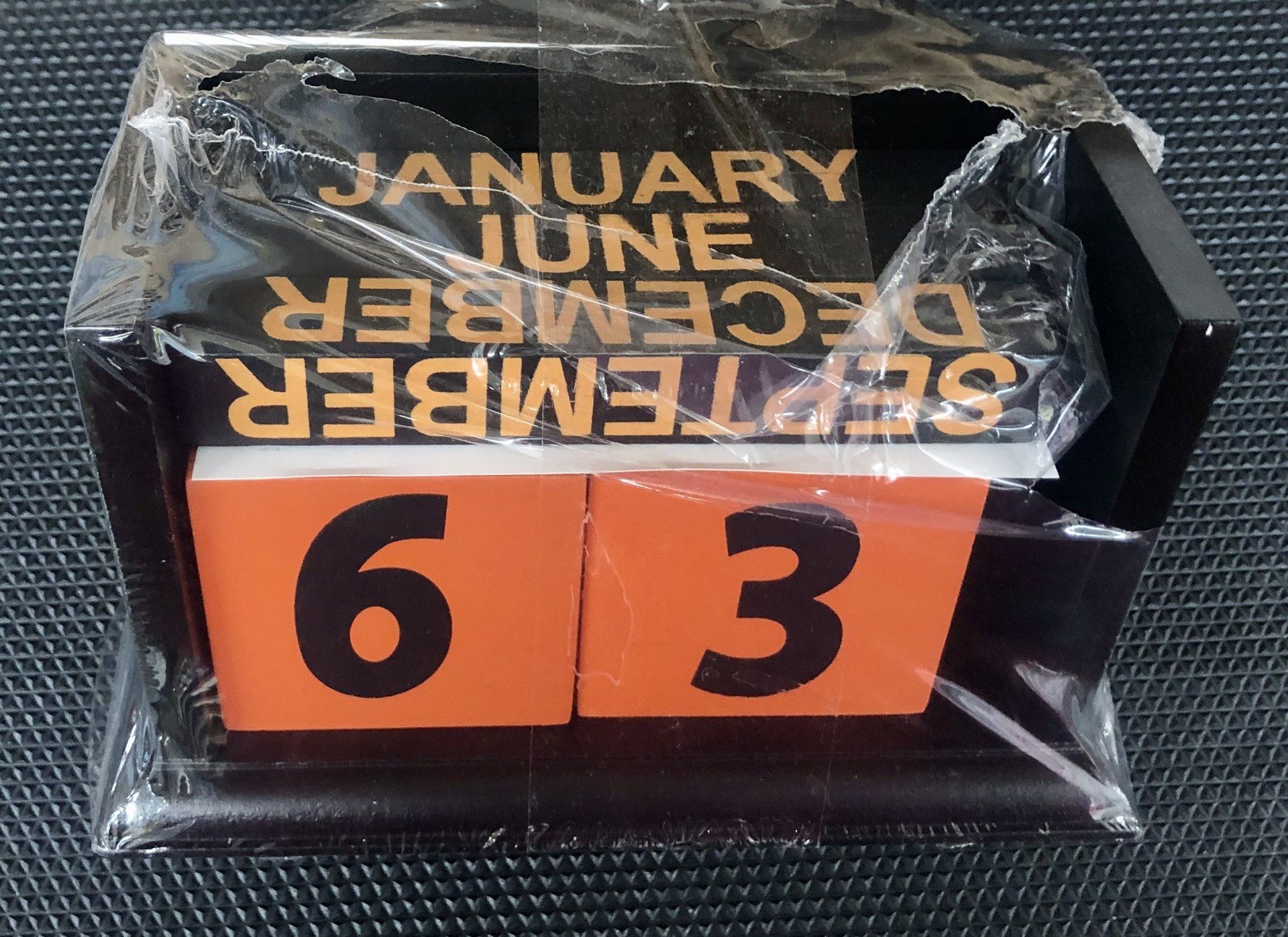 A wooden block calendar wrapped in plastic, currently showing September 63.