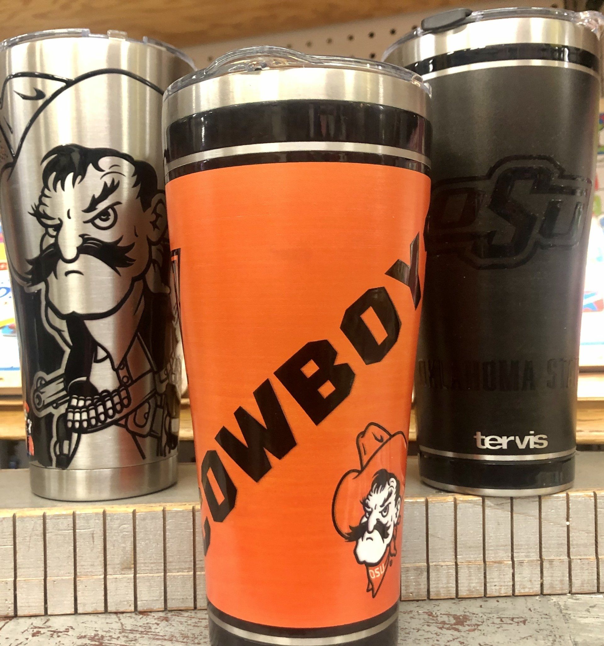 Three Tervis tumblers with Oklahoma State University Cowboy branding, arranged on a store shelf.