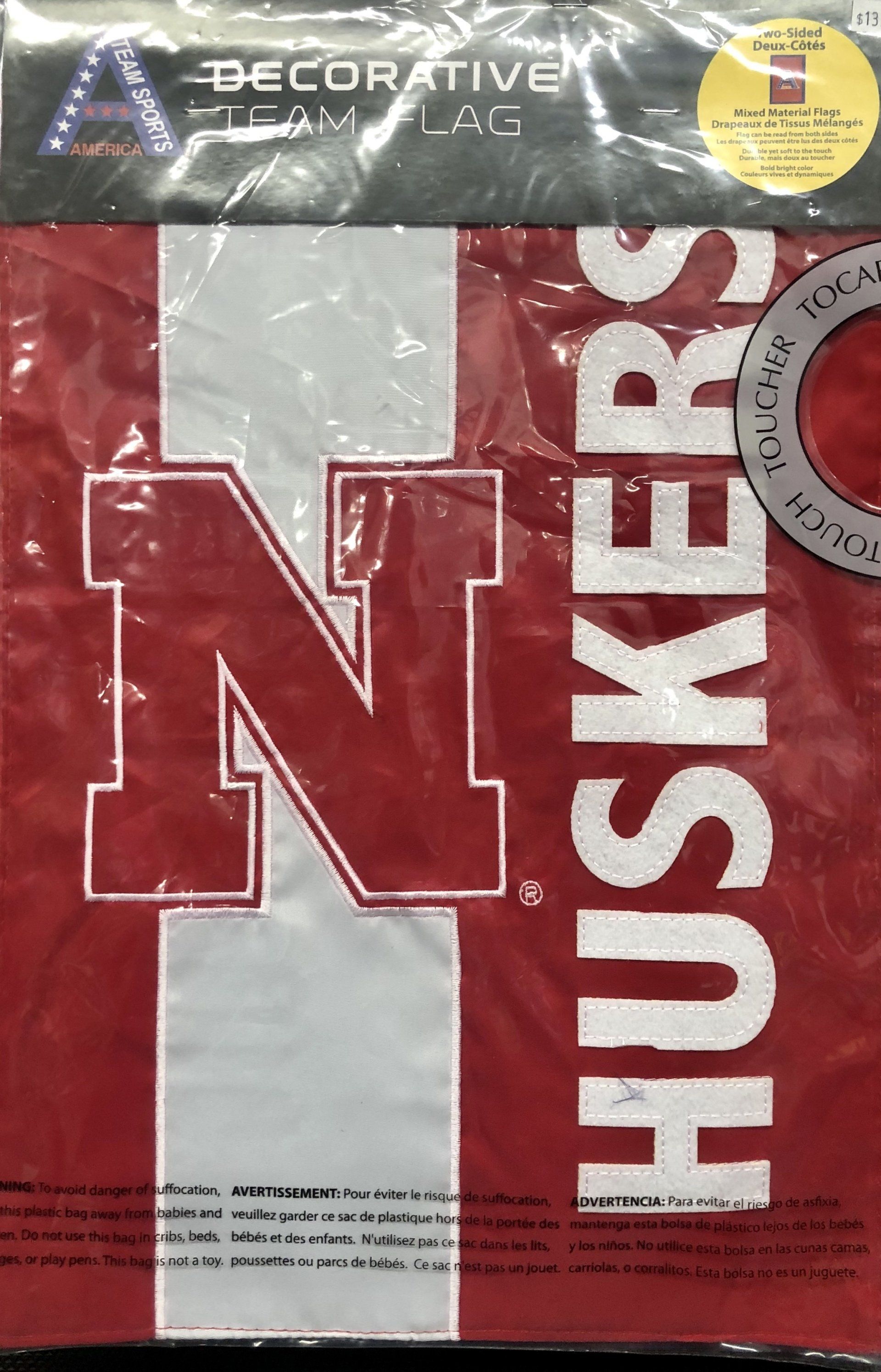 A red and white Nebraska Huskers decorative team flag in its plastic packaging.