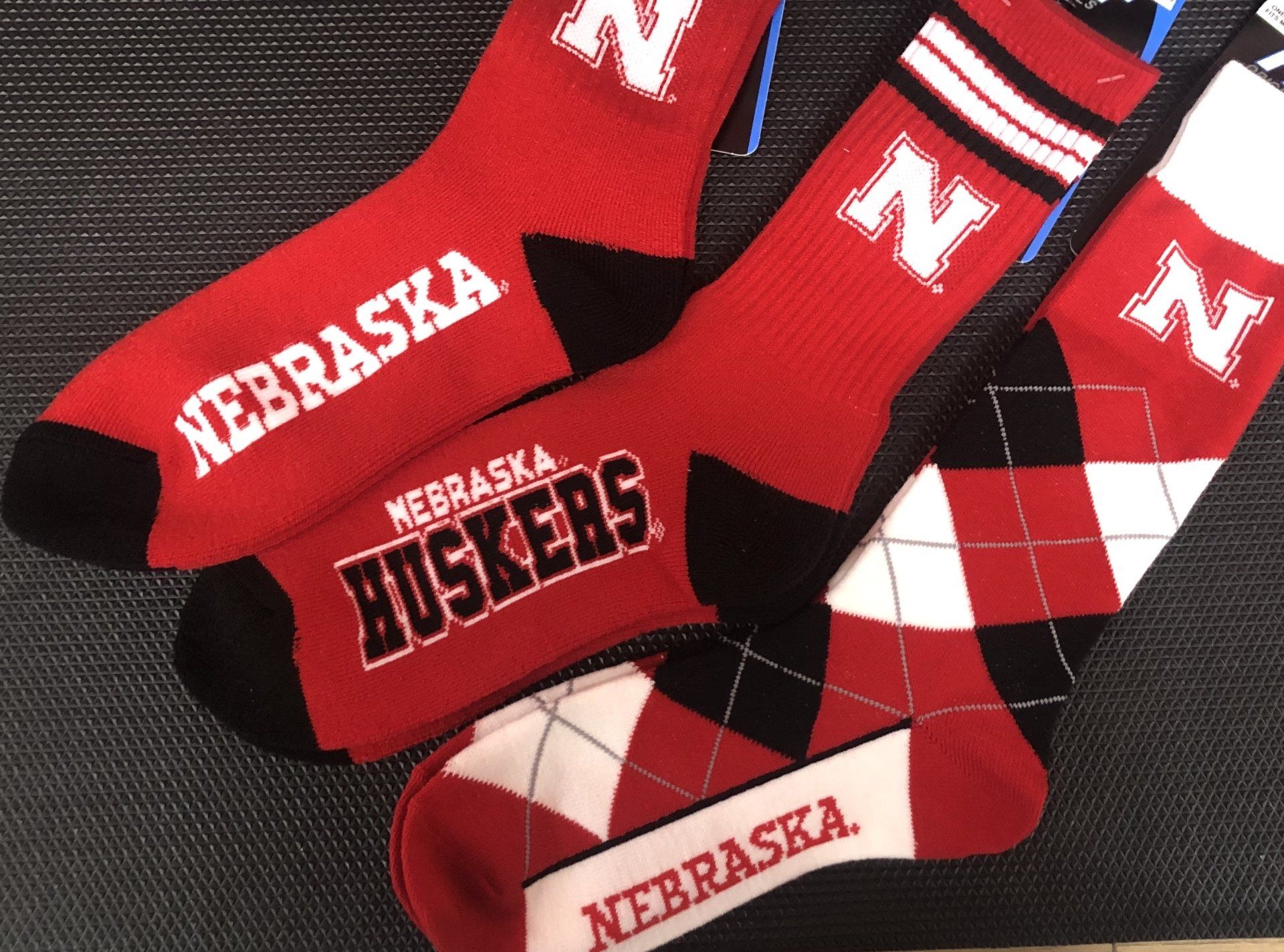 Three Nebraska Cornhuskers socks with red, white, and black designs, including a block N logo and team text.