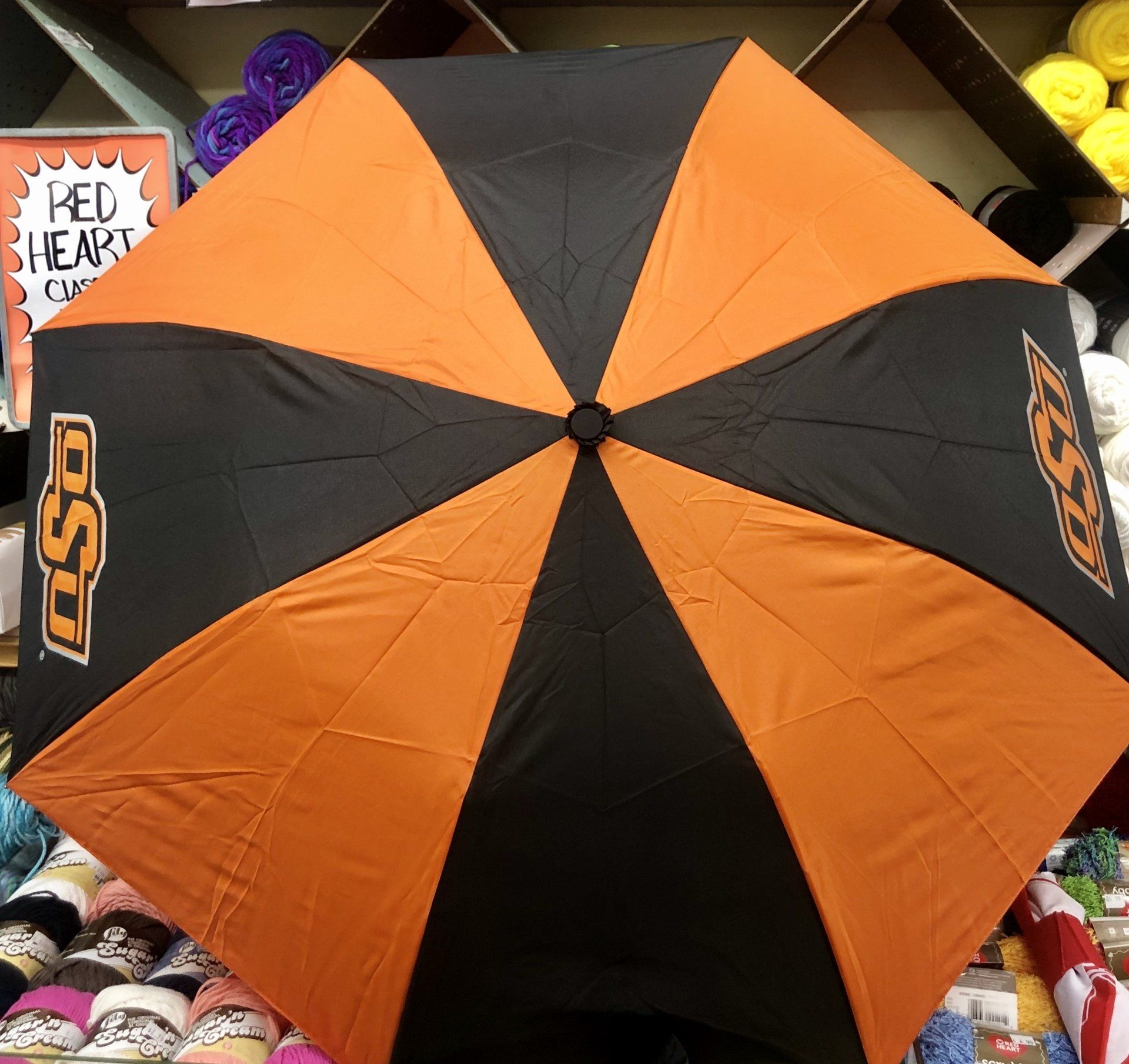 An Oklahoma State University golf umbrella with alternating black and orange panels, positioned in a craft store aisle.