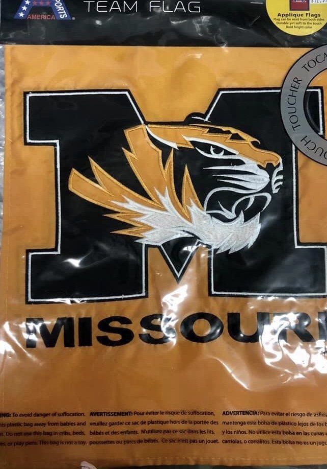 A yellow Missouri Tigers team flag in plastic packaging featuring the team logo and the word MISSOURI.