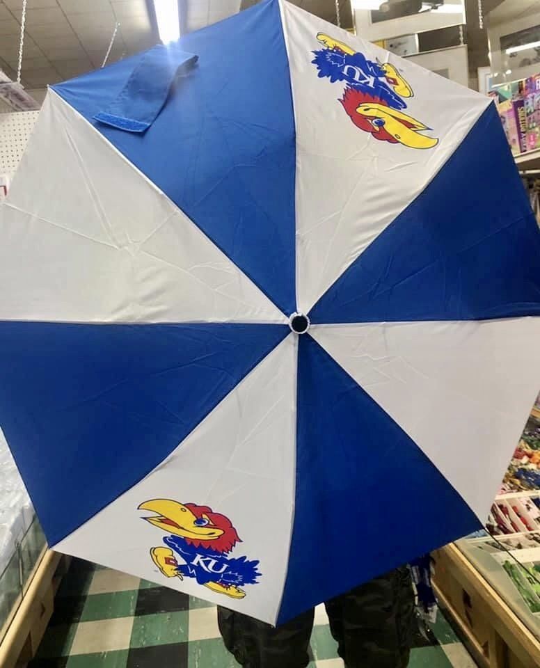 A blue and white striped umbrella featuring the Kansas Jayhawk mascot, held indoors.