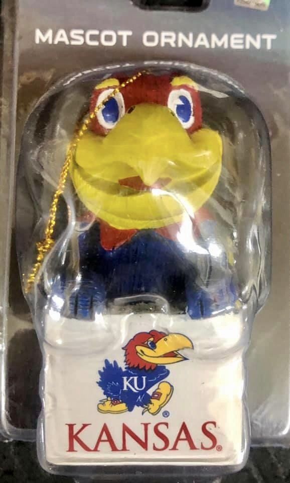 A Kansas Jayhawks mascot Christmas ornament in its original packaging, featuring the blue and yellow Jayhawk logo.