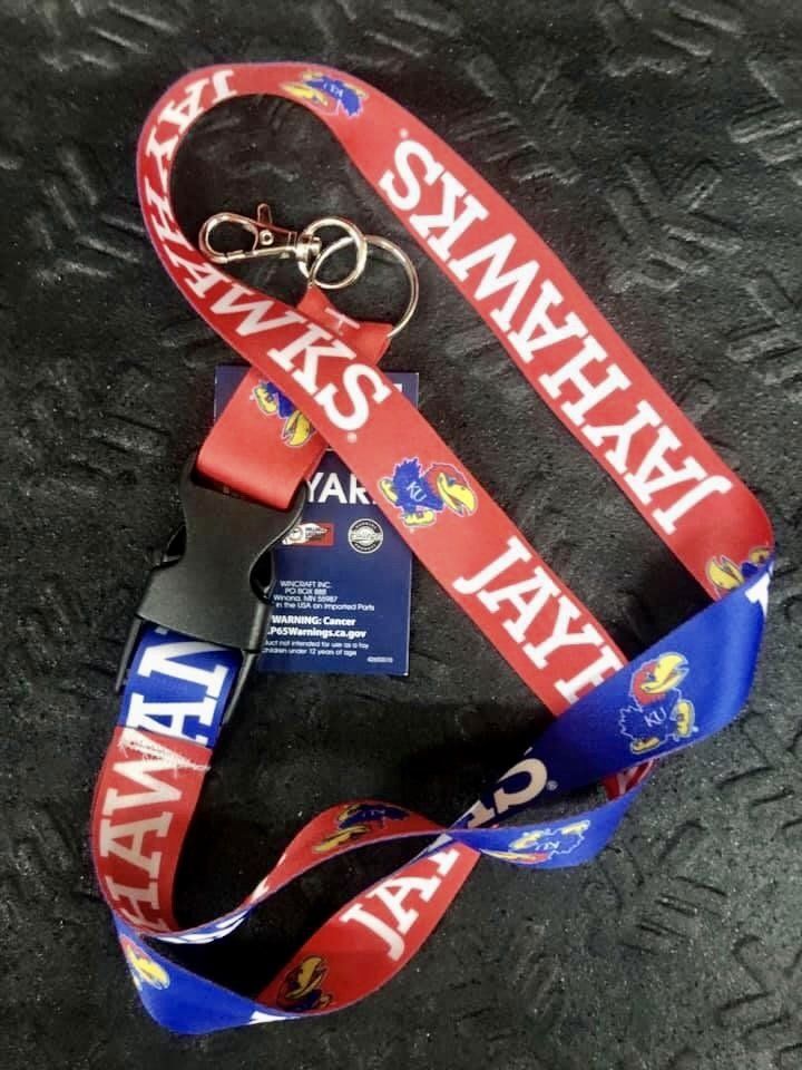 A red and blue University of Kansas Jayhawks lanyard with a black plastic buckle, key ring, and attached product tag.
