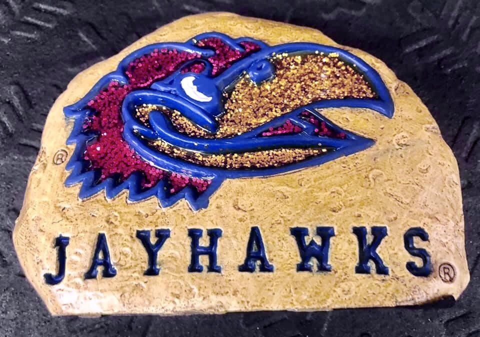 A painted stone featuring the University of Kansas Jayhawk mascot in blue, red, and gold, with 