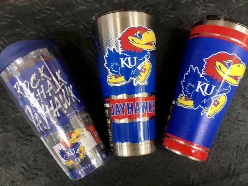 Three University of Kansas Jayhawks travel tumblers arranged on a dark, textured surface.