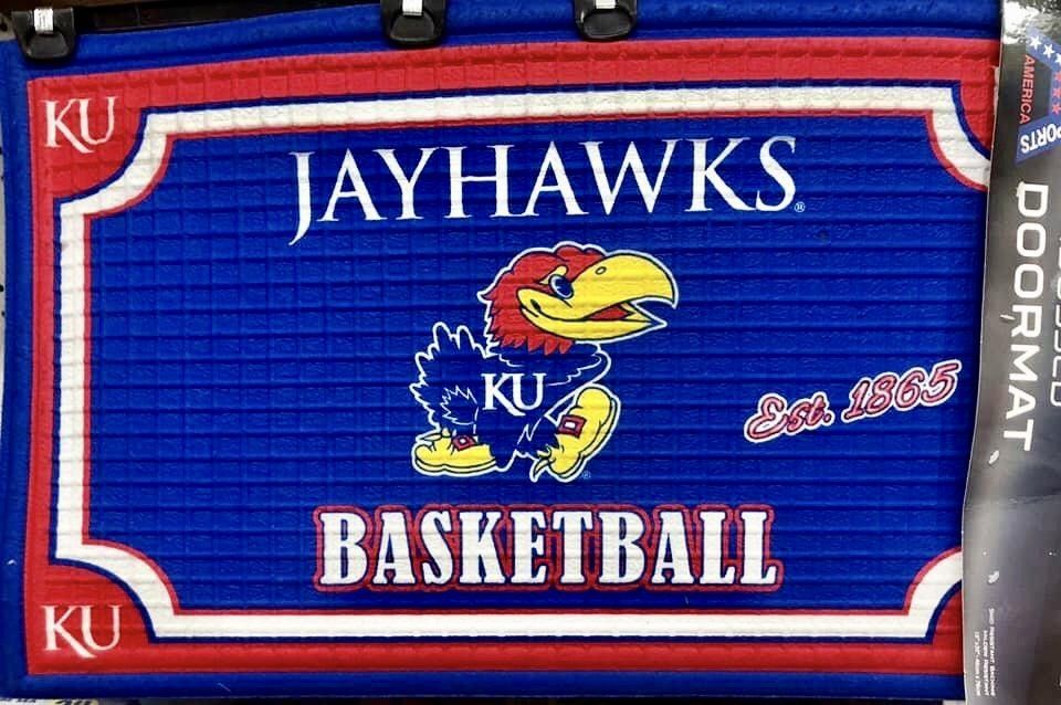 A blue rectangular Kansas Jayhawks basketball doormat with a Jayhawk mascot, text, and KU logos in red and white.