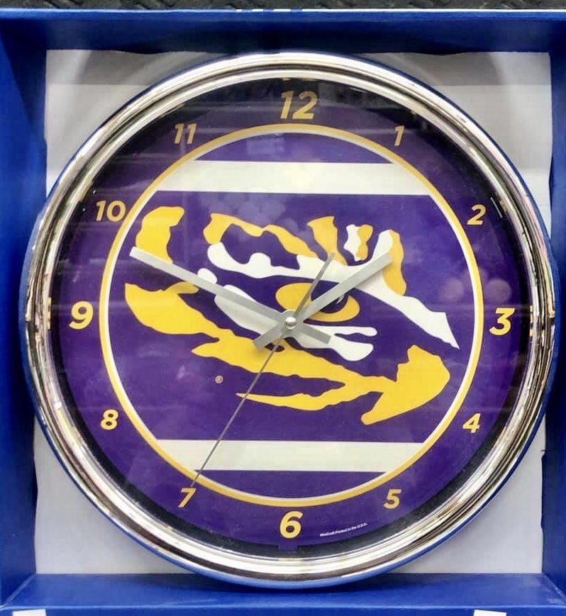A round LSU wall clock with a purple background, gold tiger logo, and metallic silver rim inside a blue box.