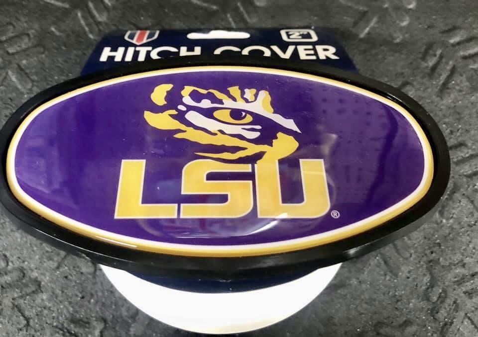 An oval LSU Tigers hitch cover with a purple background, a gold tiger eye logo, and gold text on a packaging hanger.