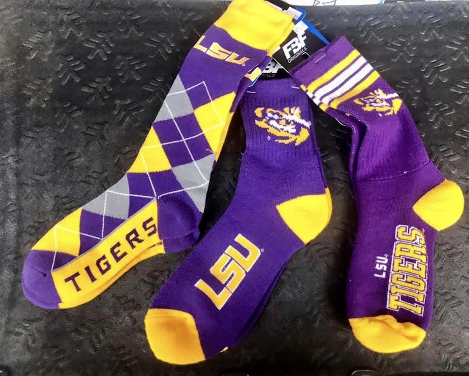 Three pairs of purple and yellow LSU Tigers themed socks displayed on a dark, textured surface.