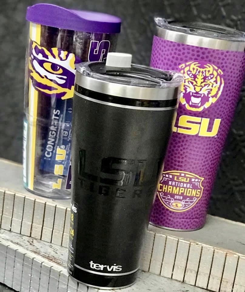 Three LSU-themed Tervis tumblers stand on a stepped surface. Two are purple and gold, and one is black.