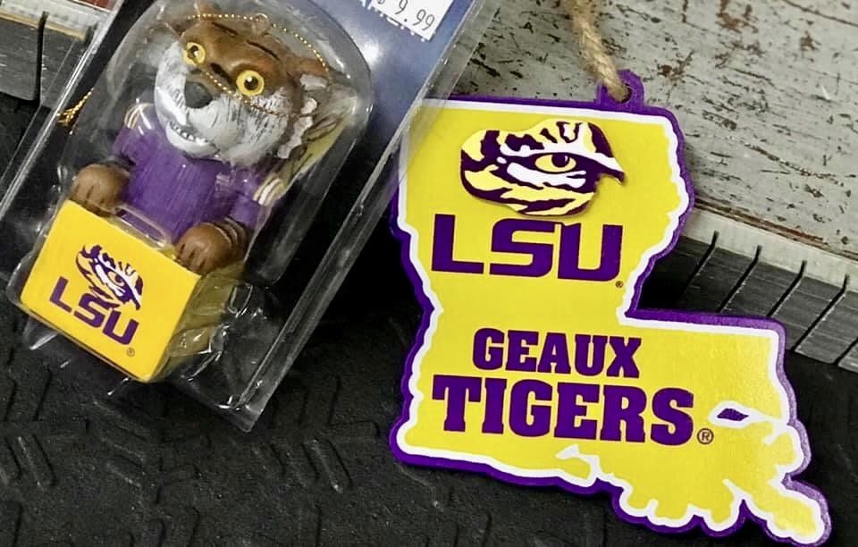 A packaged LSU tiger figurine next to an LSU-branded, Louisiana-shaped hanging ornament in purple and yellow.