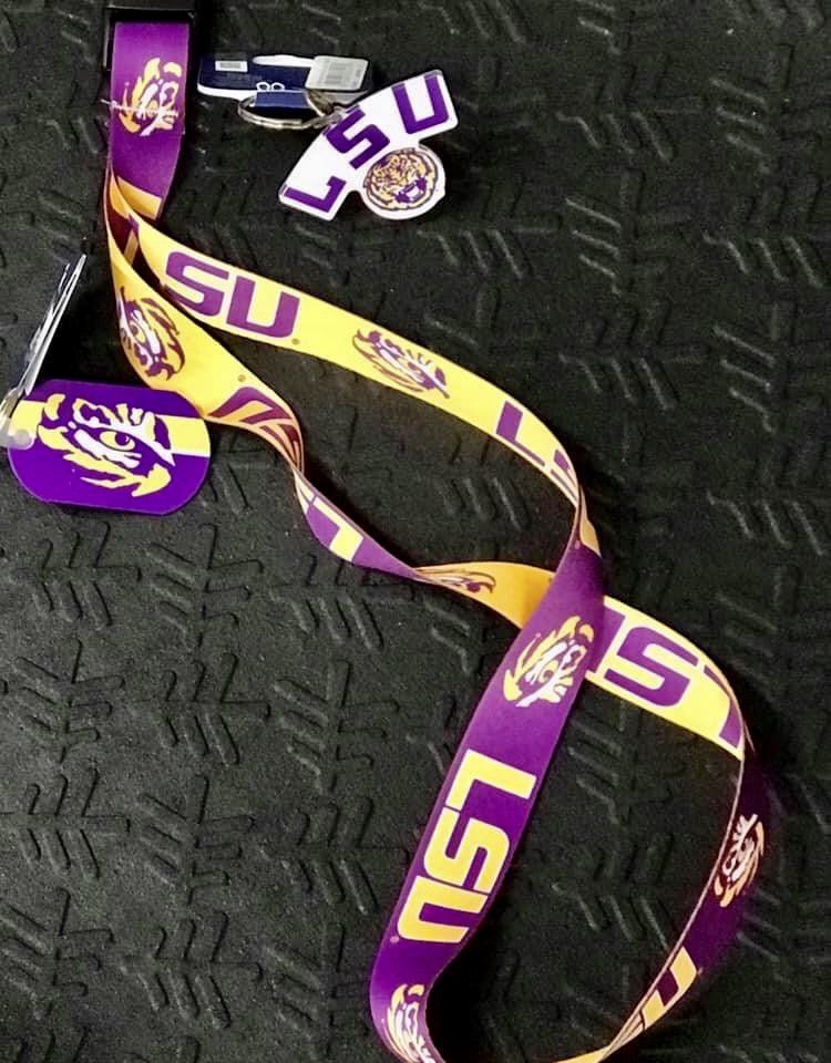 A purple and gold LSU lanyard and a matching LSU tiger head keychain resting on a dark, textured surface.