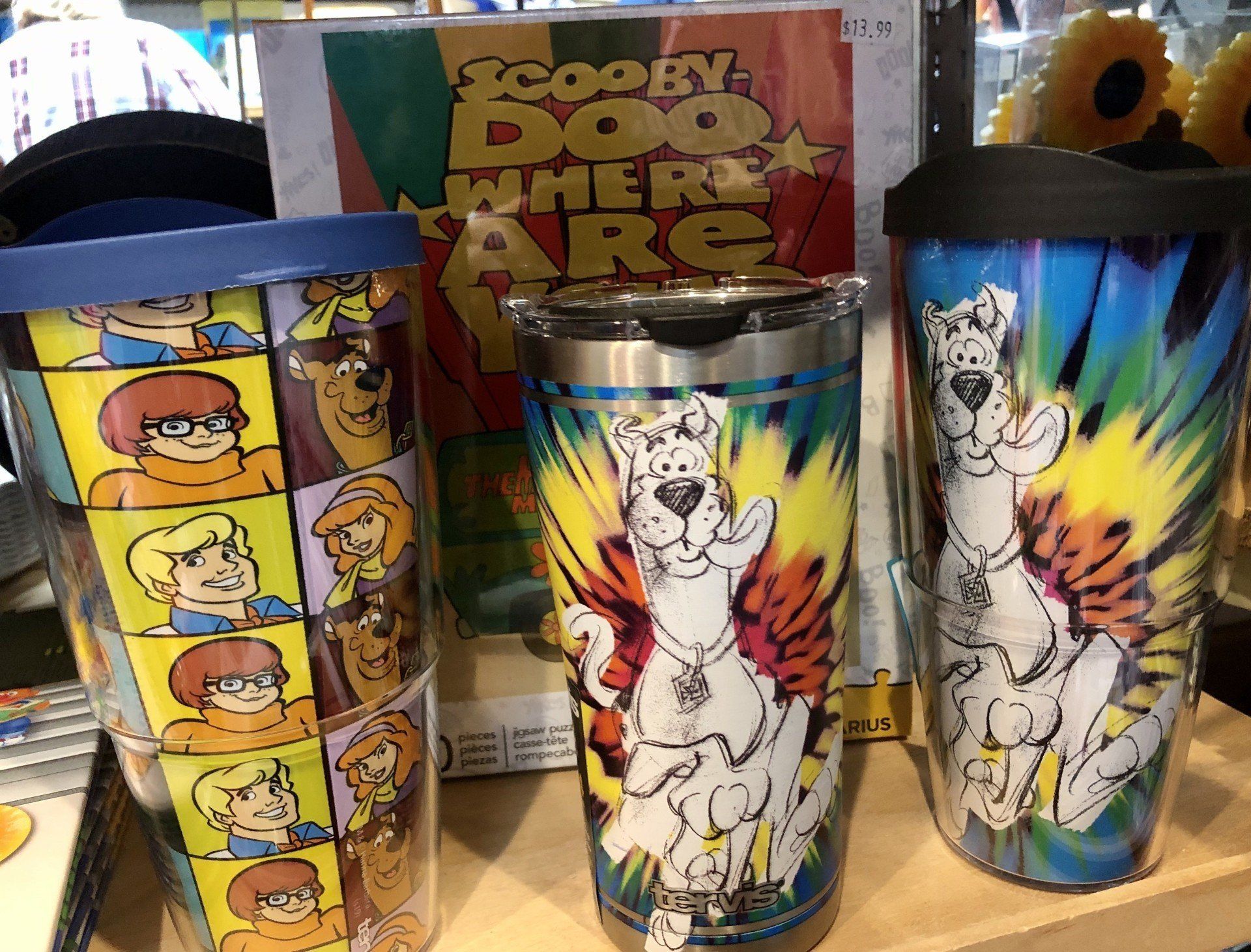 Three Scooby-Doo tumblers stand on a shelf in front of a 