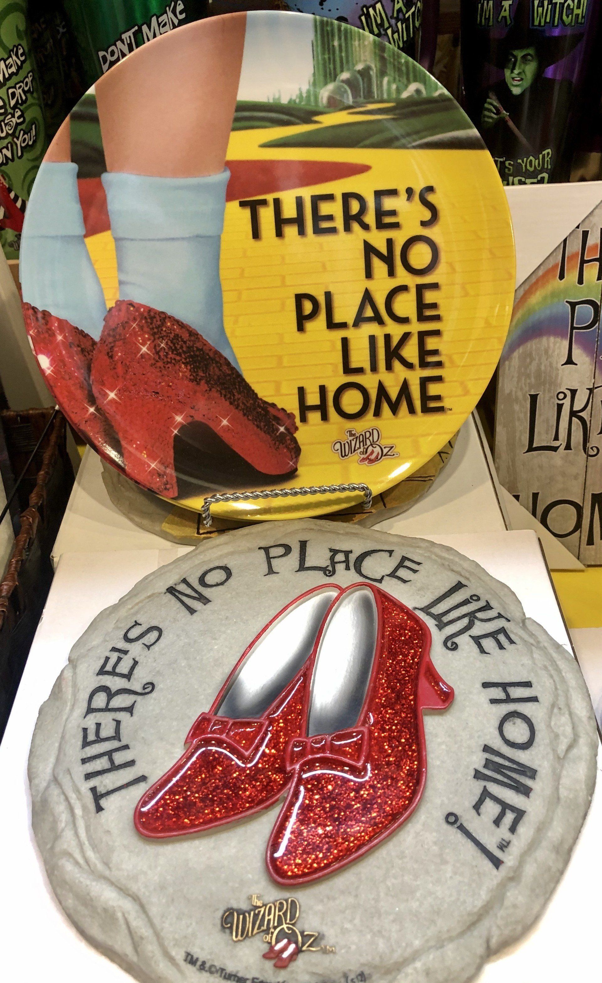 Two Wizard of Oz decorative items: a circular plate with ruby slippers on a yellow road and a stone plaque with red shoes.