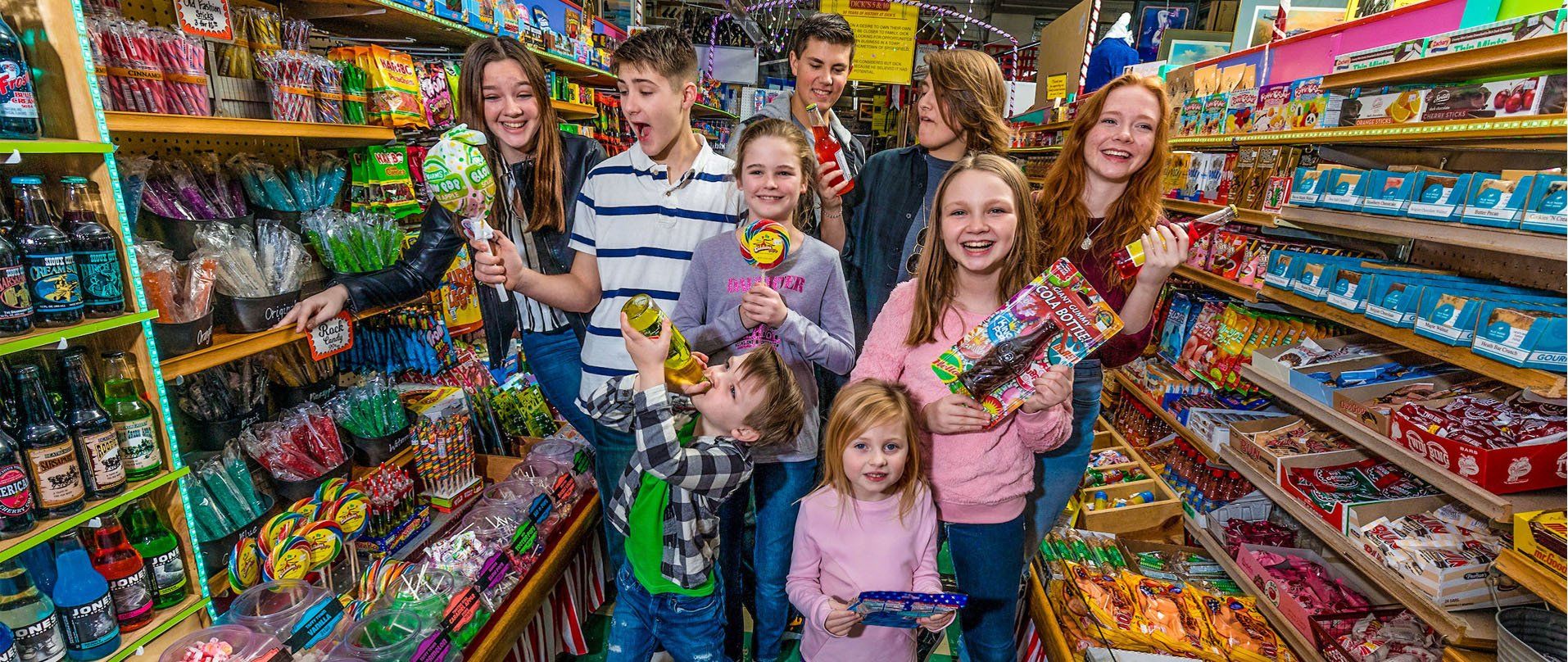 A group of people browse and hold candy in a vibrant, colorful store filled with shelves of treats.