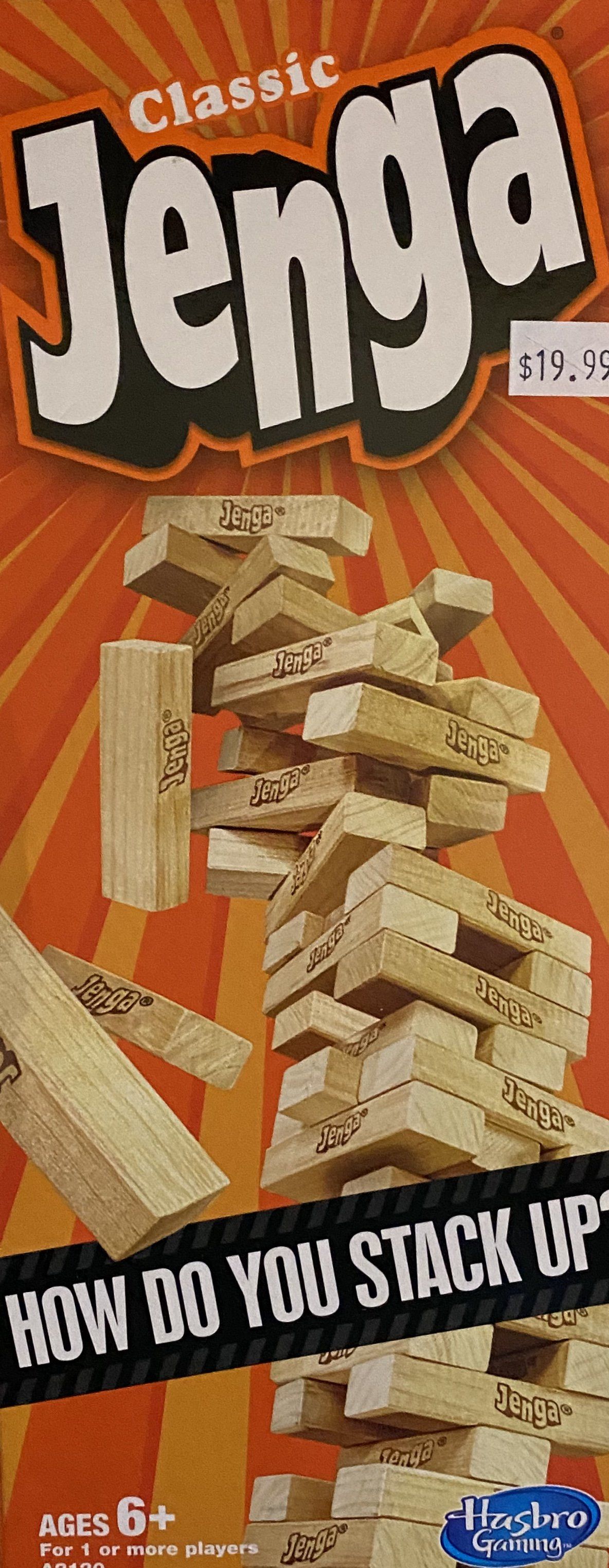 Product packaging for a Classic Jenga game featuring a tall, precarious stack of wooden blocks against an orange background.