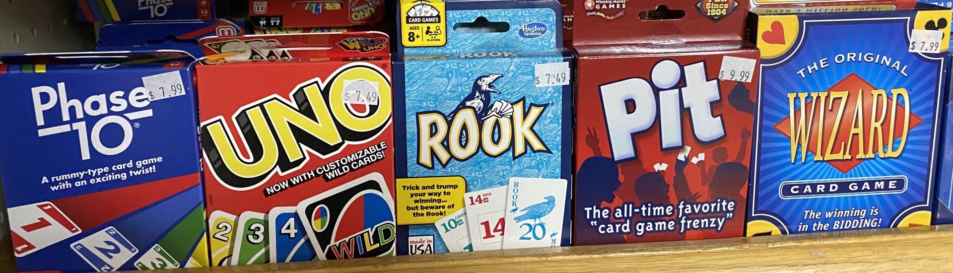 A shelf displaying five colorful boxed card games: Phase 10, Uno, Rook, Pit, and Wizard.