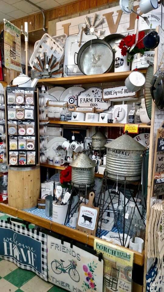A retail display shelf filled with farmhouse-style decor, including metal basins, small silos, and various home signs.
