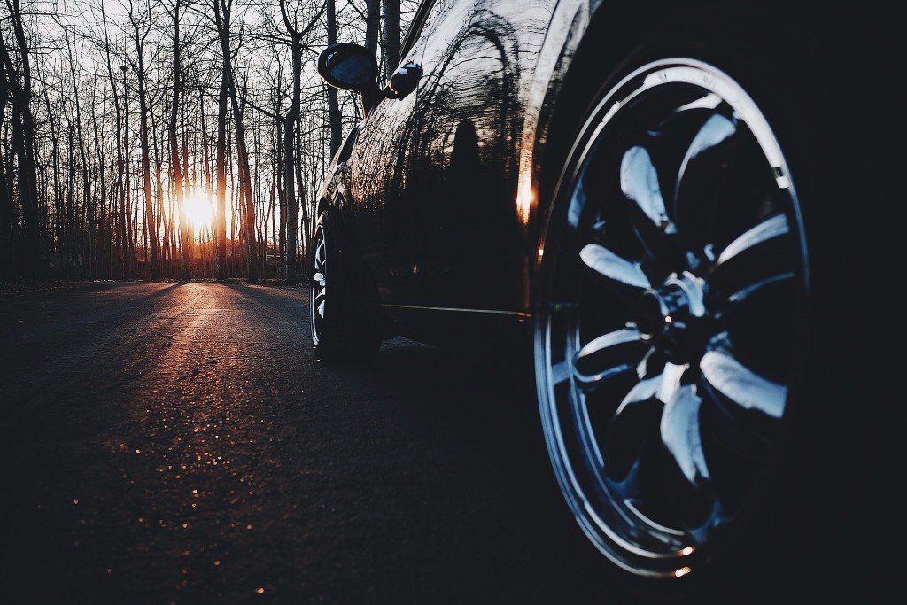 A car is parked on the side of the road with the sun shining through the trees in the background.