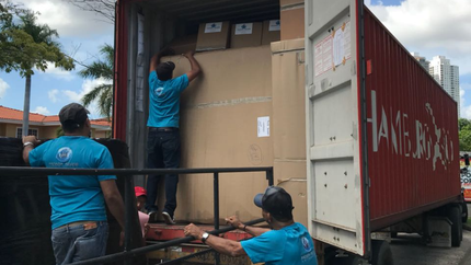Trabajadores descargando grandes cajas de cartón de un contenedor marítimo en el muelle de un almacén