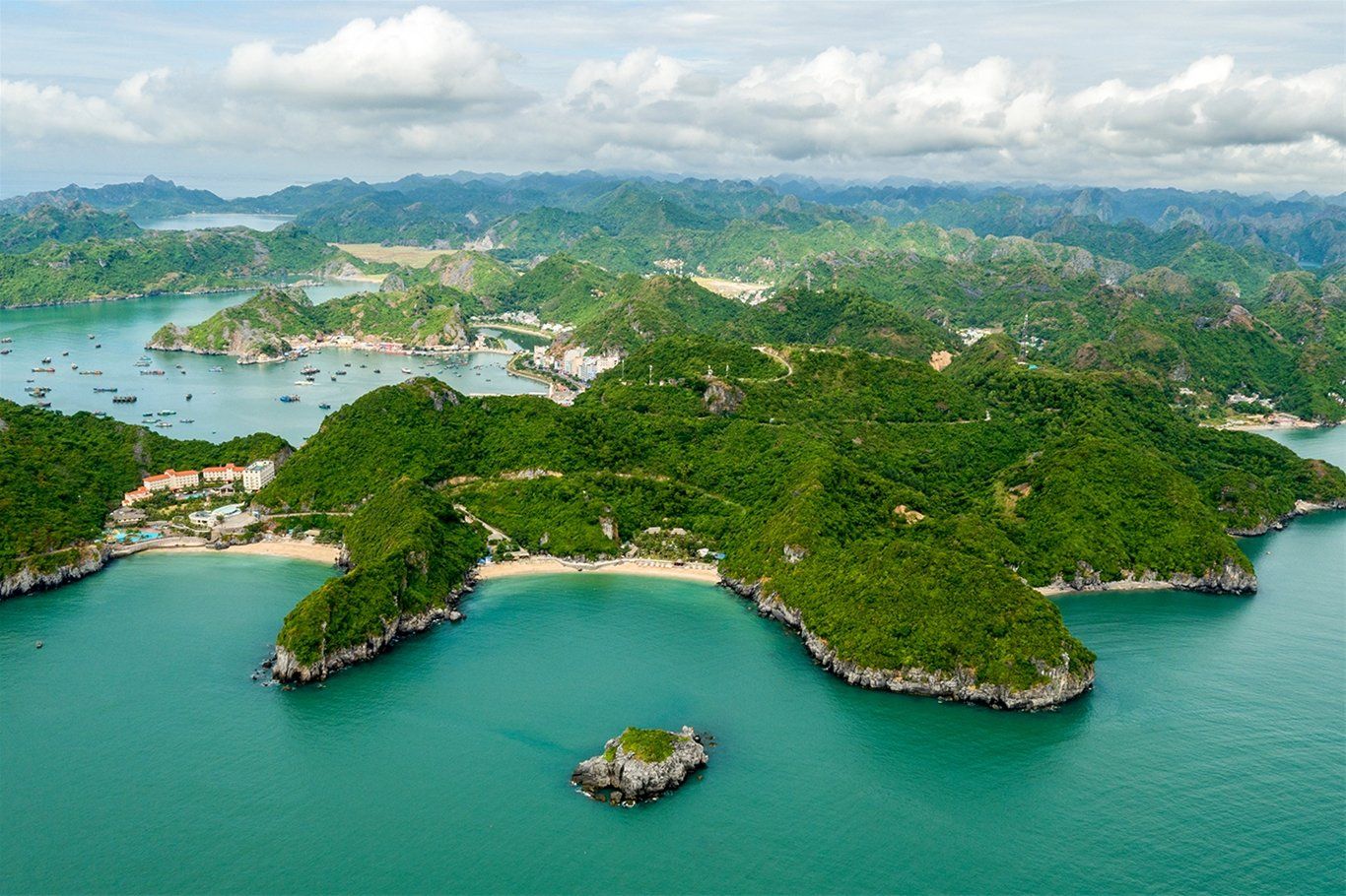 An aerial view of a small island in the middle of a large body of water surrounded by mountains.