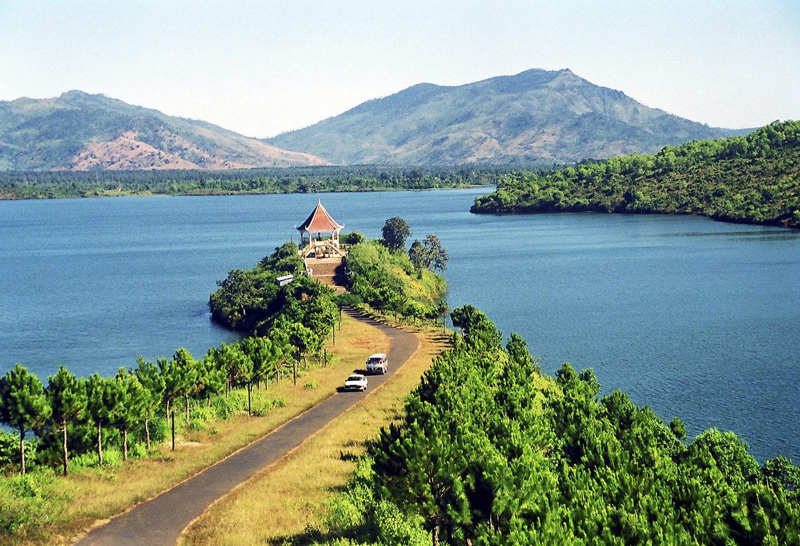 Cars are driving down a road next to a lake with mountains in the background