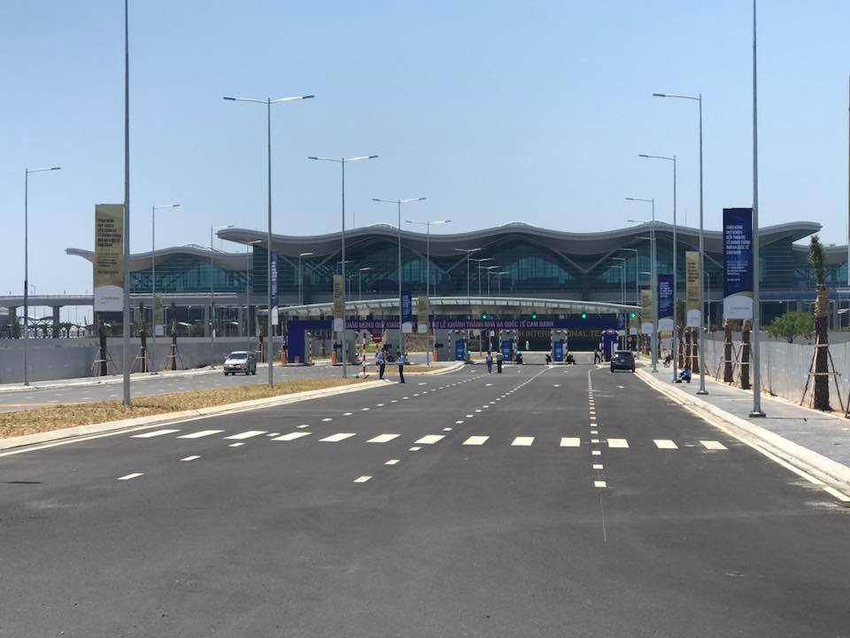 A road leading to an airport with a large building in the background.