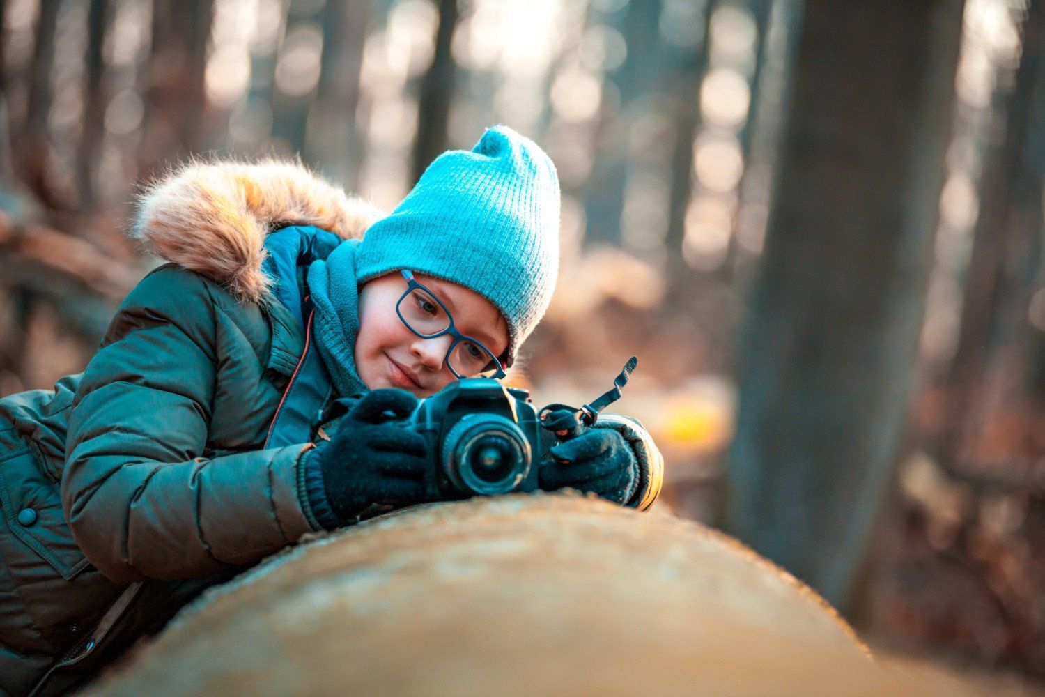 A young boy is taking a picture with a camera in the woods.
