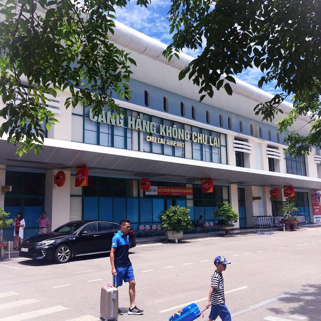 A man carrying a suitcase walks down a street in front of a building that says hang khom