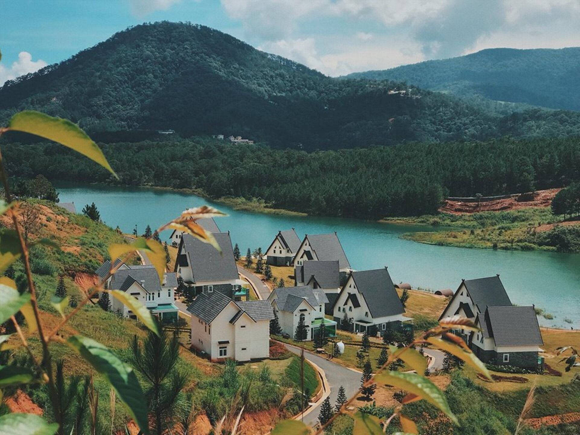 A small village on a hill next to a lake with mountains in the background.