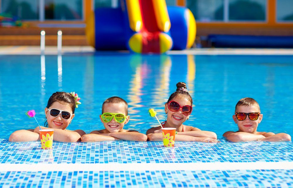 A group of children are sitting on the edge of a swimming pool.
