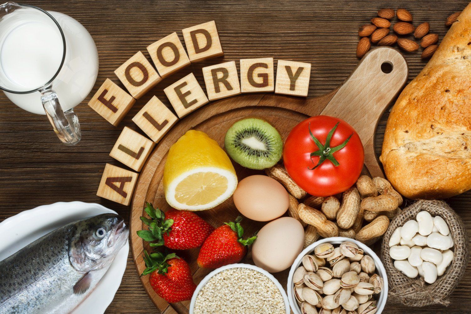 A wooden cutting board topped with a variety of foods including fish , vegetables , nuts and bread.