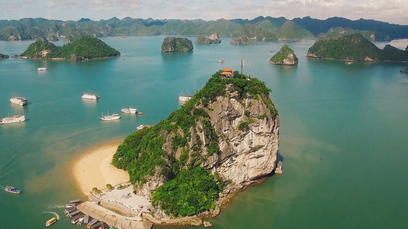 An aerial view of a small island in the middle of a large body of water surrounded by boats.