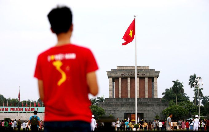 A man in a red shirt with the number 3 on it stands in front of a flag.