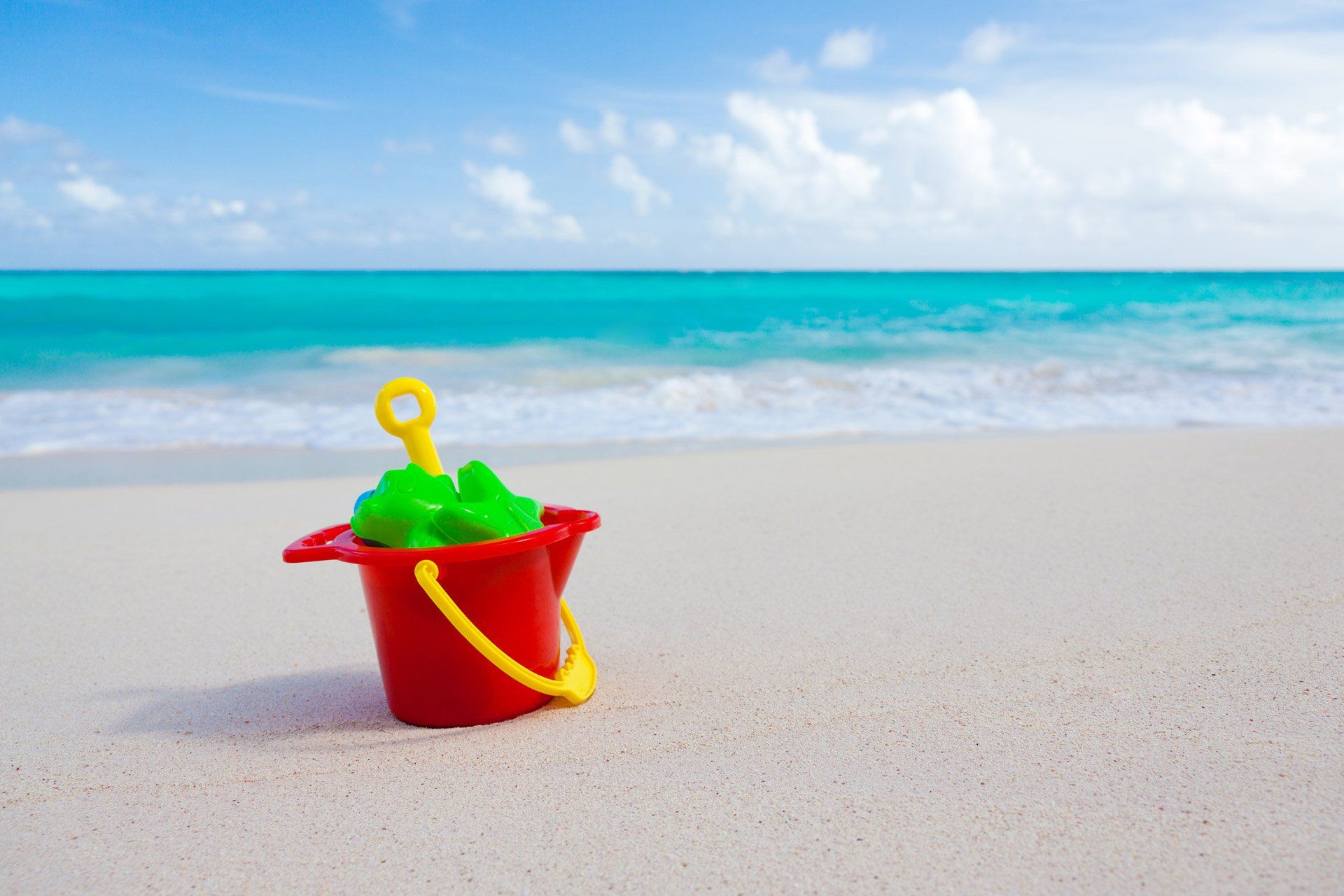 A red bucket with green sand castles in it on the beach