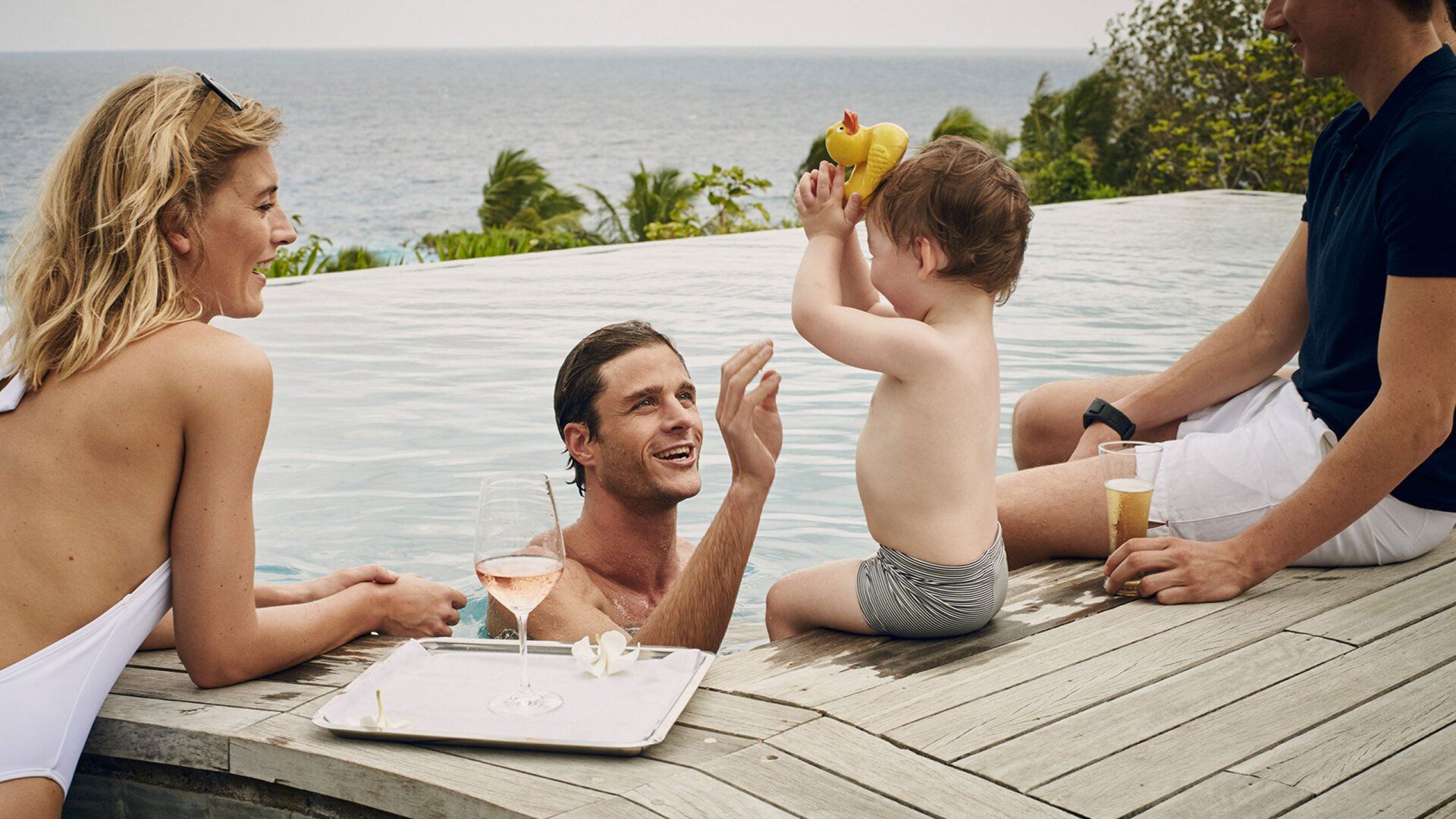 A family is sitting on the edge of a swimming pool.