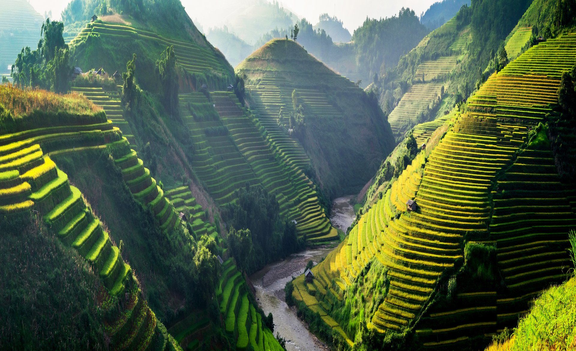 A river runs through a valley surrounded by mountains and terraced fields.