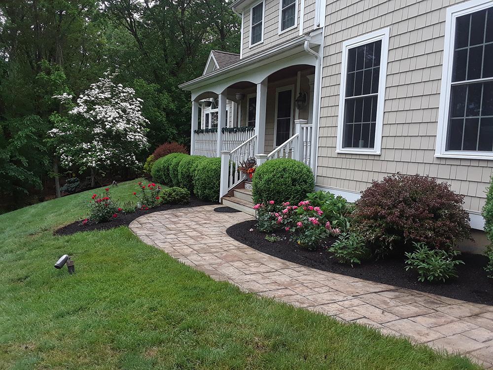 Front walkway and flower beds beside a beige house with white trim and a small porch.