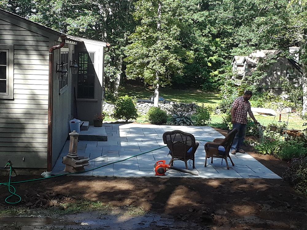 Backyard patio under construction with concrete slab, tools, and a person working near a shed