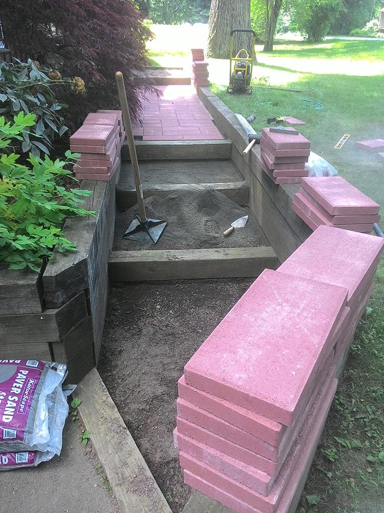 Partially built outdoor steps with stacked pink pavers and a garden path in the background