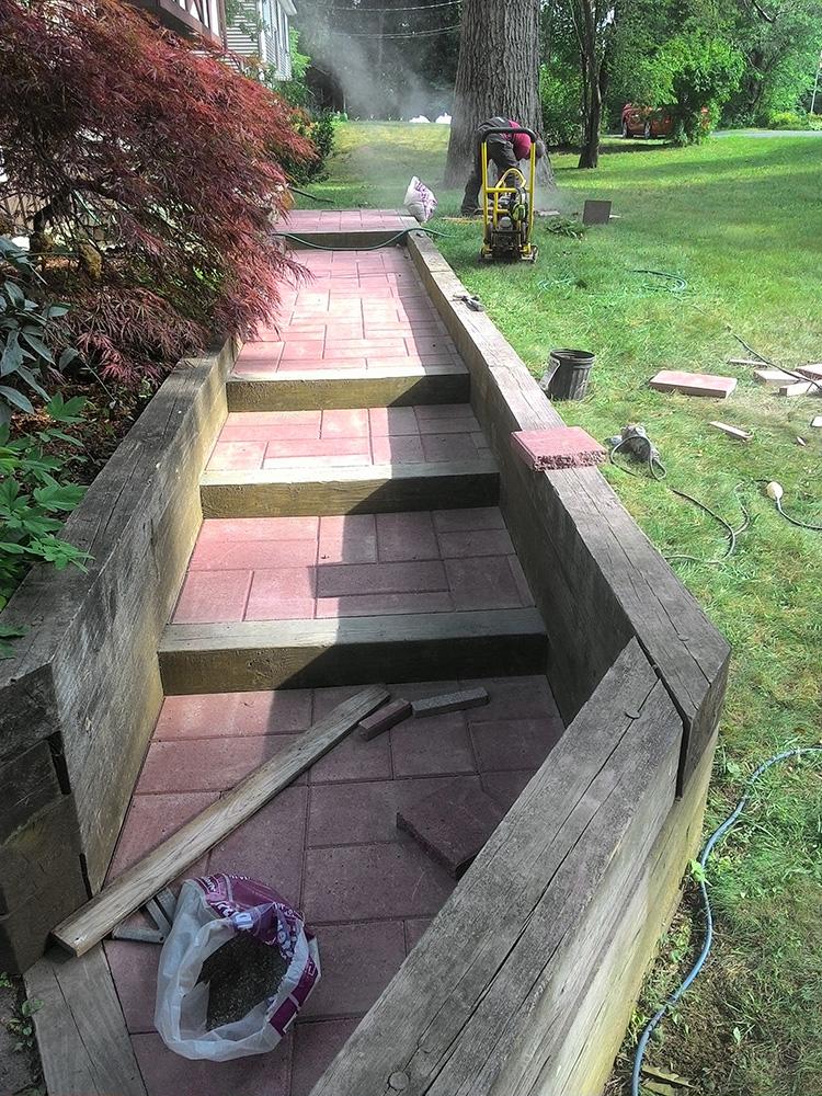 Broken outdoor stone walkway with uneven steps, construction debris, and a grassy park beside it