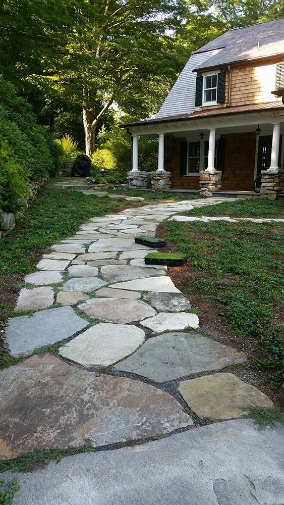 Stone garden path leading to a house porch surrounded by trees and greenery