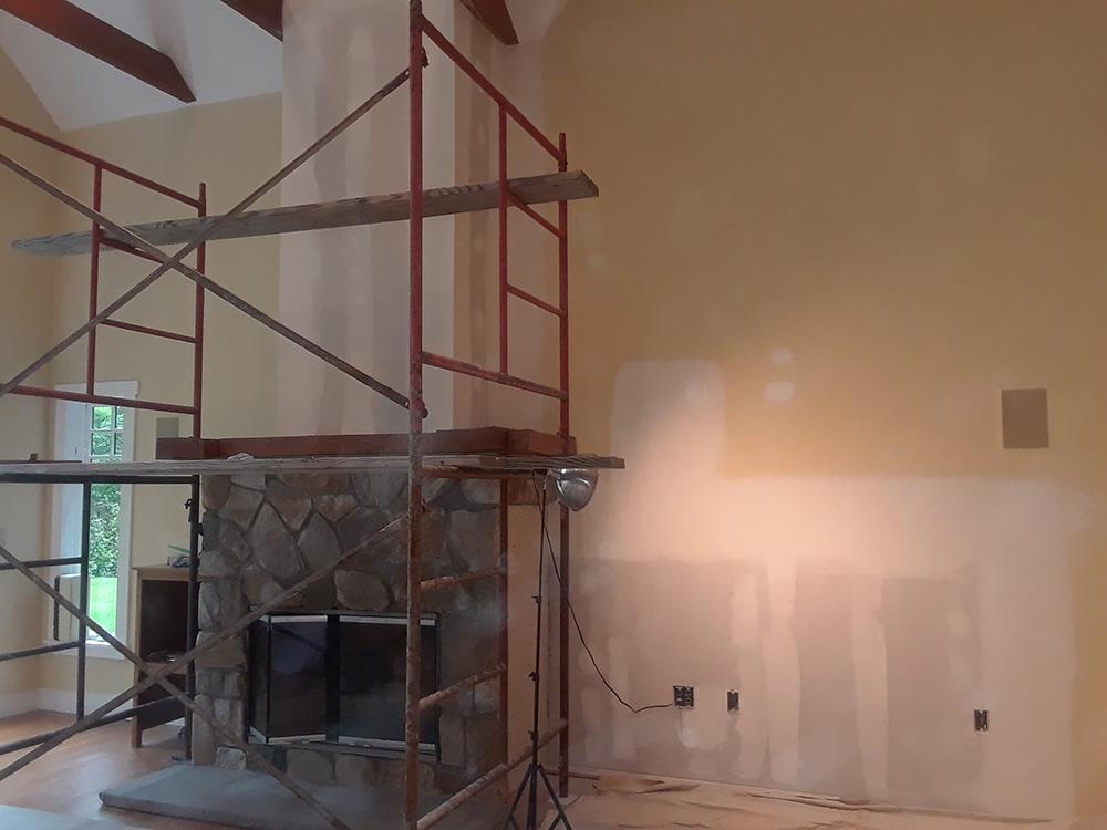 Scaffolding in a living room beside a stone fireplace and partially painted wall