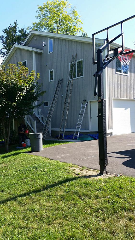 Backyard house exterior with ladders against the wall and a basketball hoop on the driveway