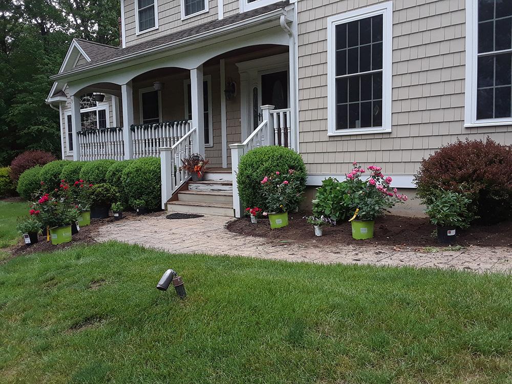 Front porch of a gray house with white trim, flower beds, and a green lawn in front.