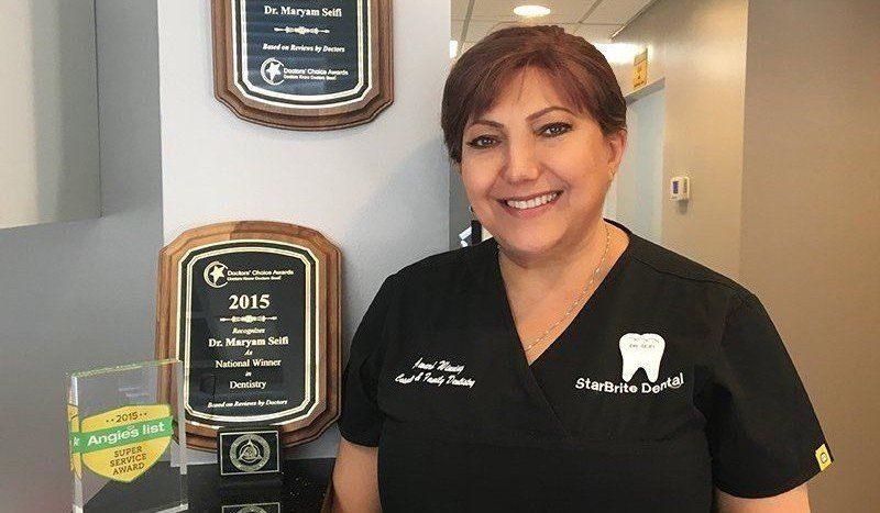 A woman in a black scrub top is standing in front of two plaques.