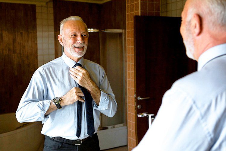 An older man is adjusting his tie in front of a mirror.